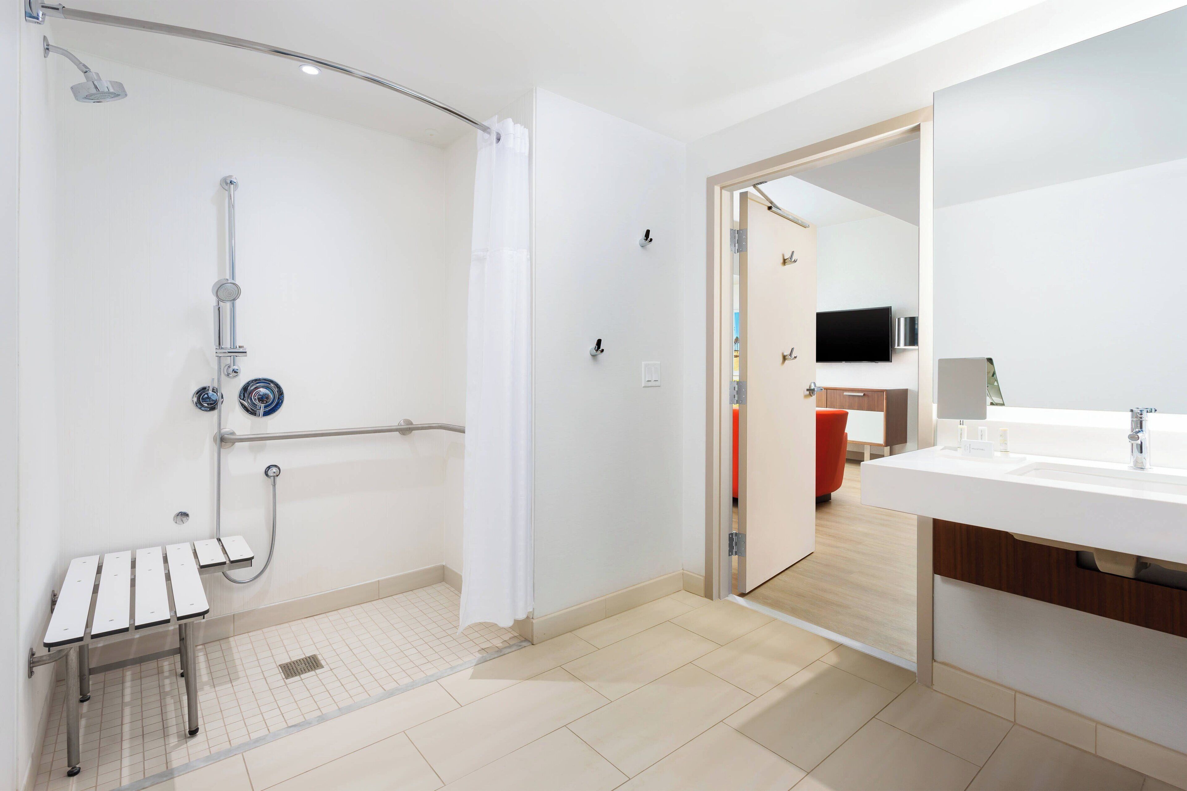 A modern bathroom with a shower, a bench, a sink, and a mirror.
