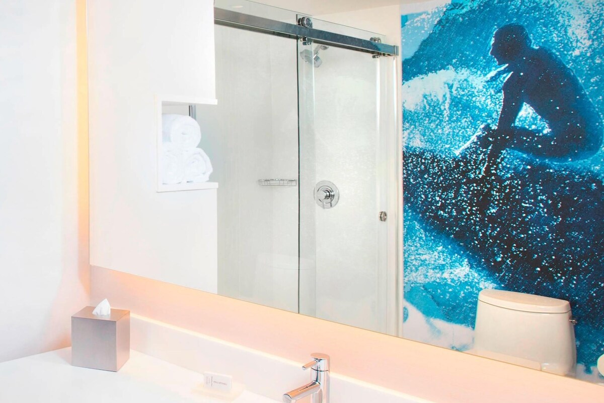 A modern bathroom with a large mirror, a glass shower enclosure, and a sink with toiletries.