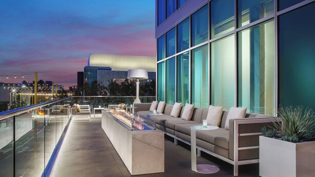A rooftop lounge with a modern design, featuring a long bar, comfortable seating, and large windows offering city views. - Courtyard by Marriott Santa Monica (Santa Monica)