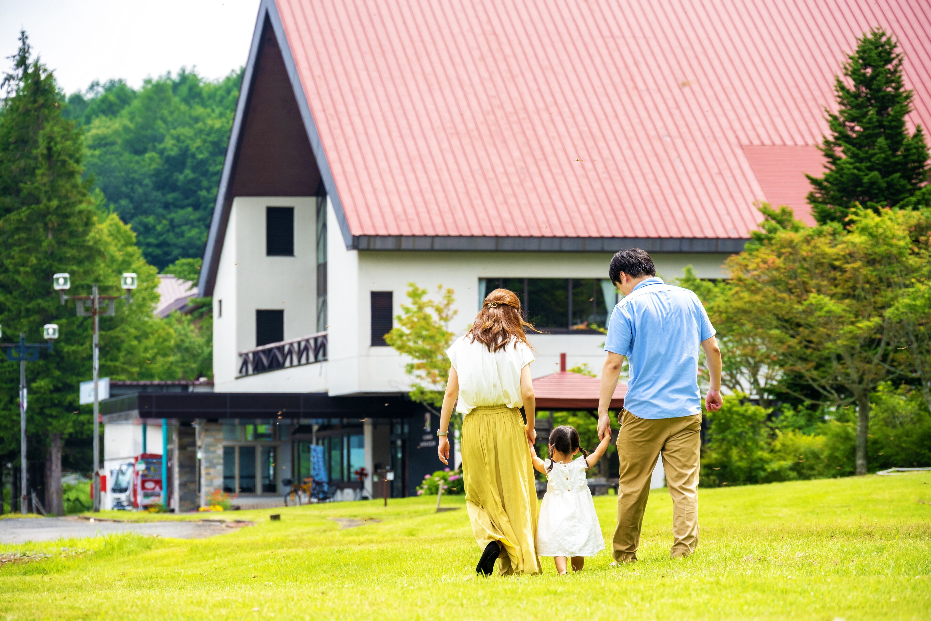 A family walking on a grassy lawn in front of a building with a red roof.