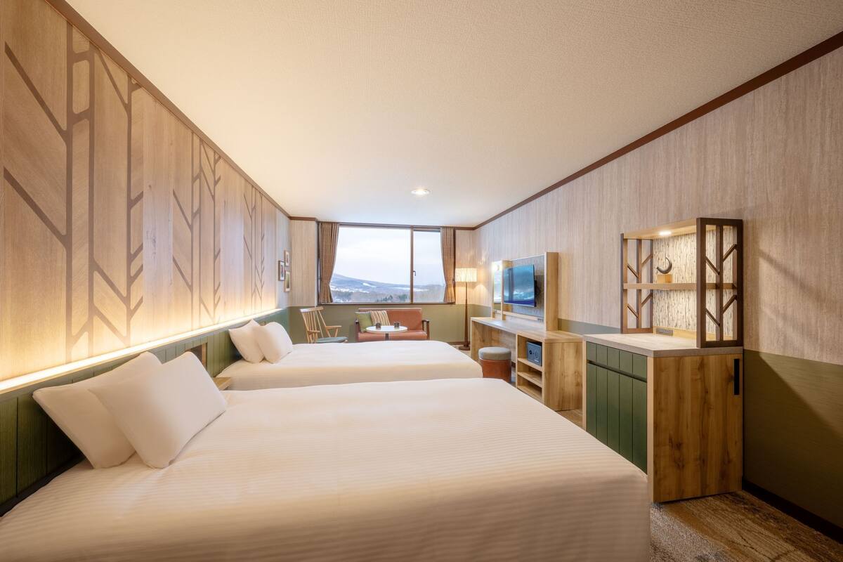 A hotel room with two beds, a desk, a TV, and a view of the outdoors.