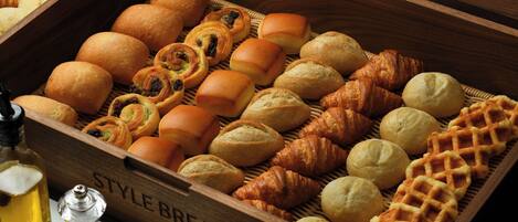 A wooden box filled with various breads and pastries, including croissants and rolls.