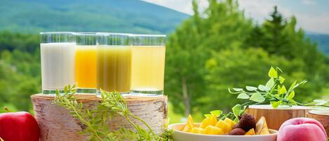 A wooden table with three glasses of juice, a bowl of fruit, and apples.