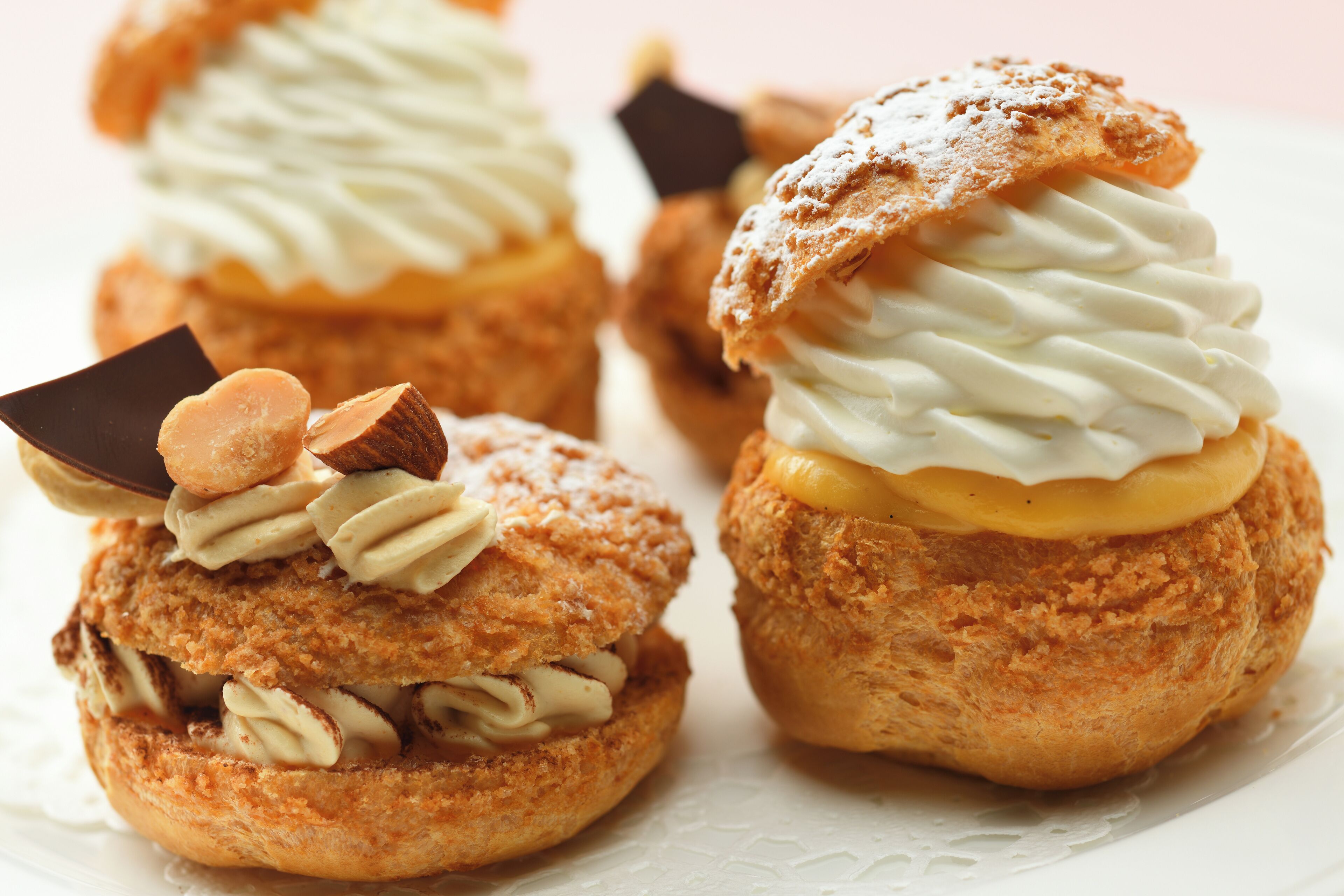 Tres profiteroles con crema batida y trozos de chocolate sobre un plato blanco.