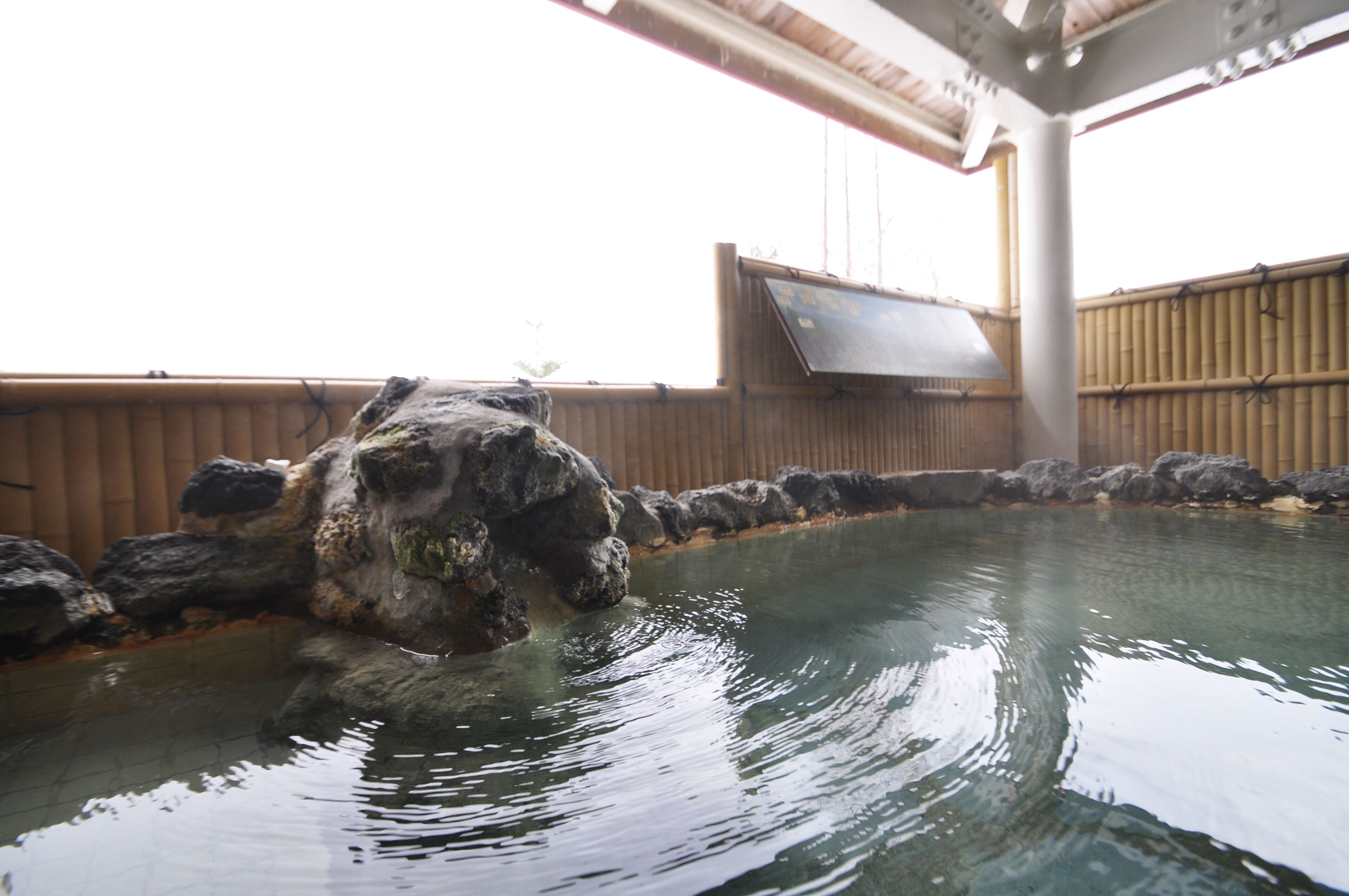 Une piscine bordée de rochers, avec une clôture en bambou en arrière-plan.