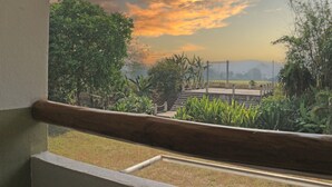 A balcony with a view of a sunset over a park with trees and a distant hill.