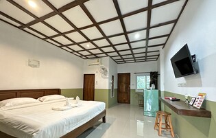 Habitación de hotel con una cama grande, techo de madera, televisor montado en la pared y un taburete pequeño.