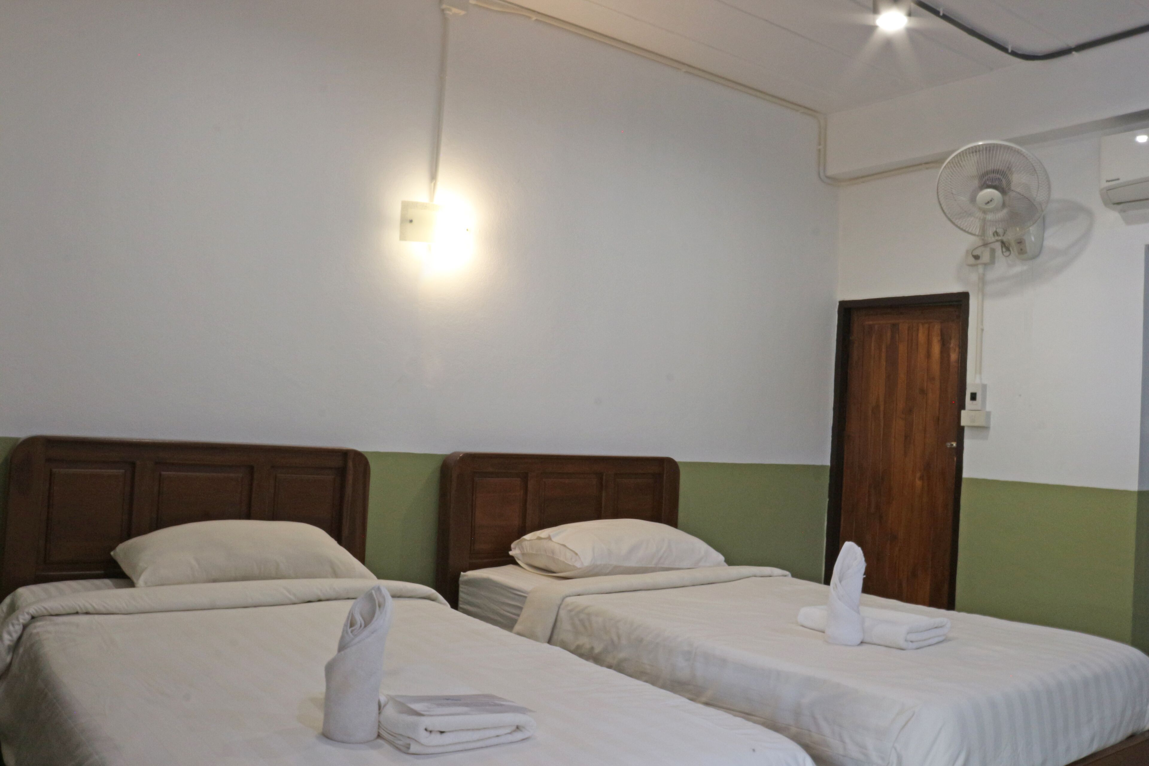 Habitación de hotel con dos camas individuales, cabecera de madera, ventilador de pared e iluminación colgante.
