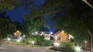 A nighttime view of a lodge with multiple cabins, surrounded by trees and illuminated by exterior lights.