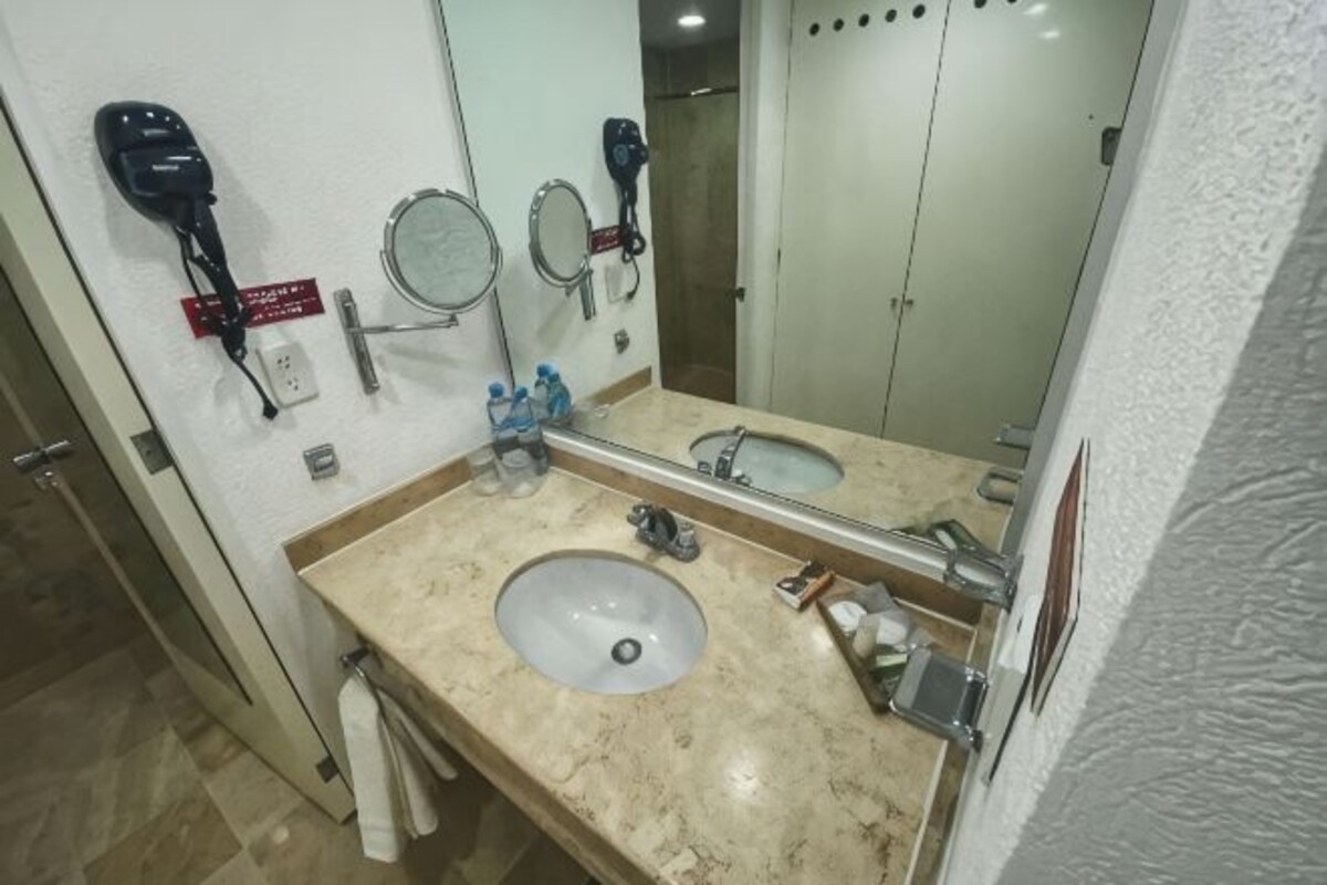 A bathroom with a sink, two mirrors, a hairdryer, and a towel rack.