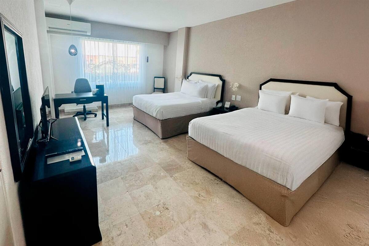 A hotel room with two beds, a desk, a chair, and a TV.