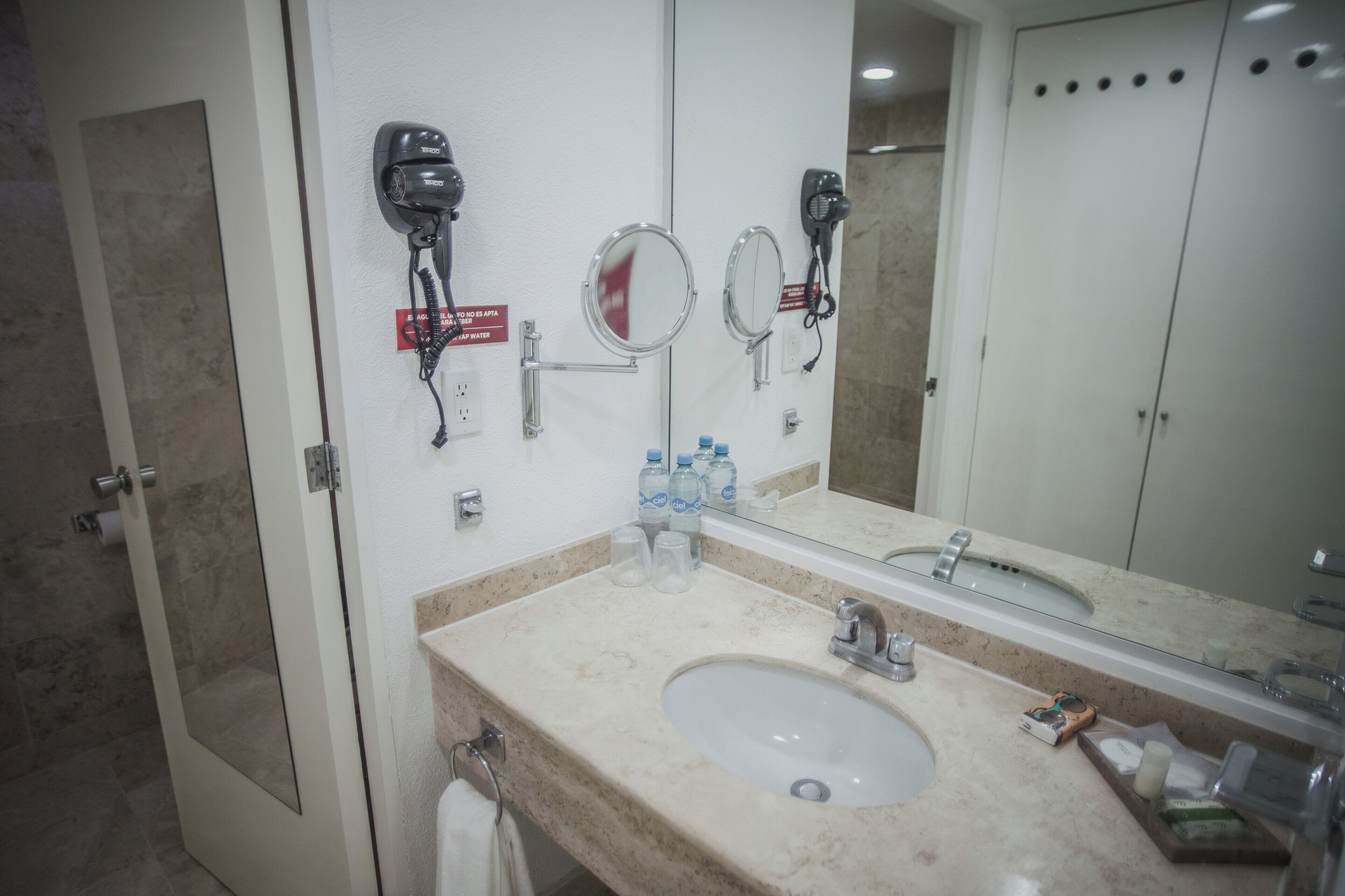 A bathroom with a sink, mirror, hair dryers, and toiletries.