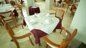 Comedor con mesas redondas dispuestas para cuatro, cada una con mantel blanco y sillas de madera.