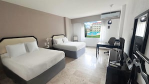 Habitación de hotel con dos camas, un escritorio, una silla, un televisor y ventana con vista a una piscina.