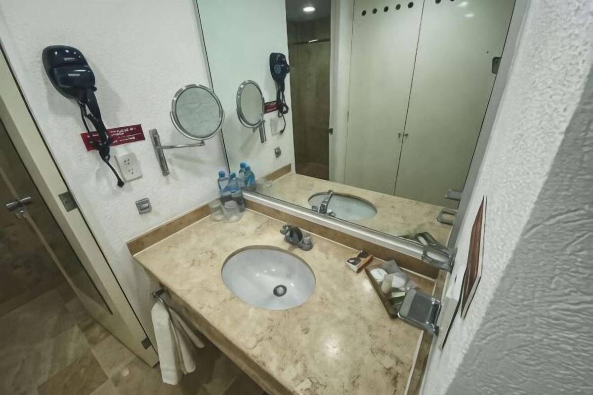 A bathroom with a sink, two mirrors, a hairdryer, and a towel rack.