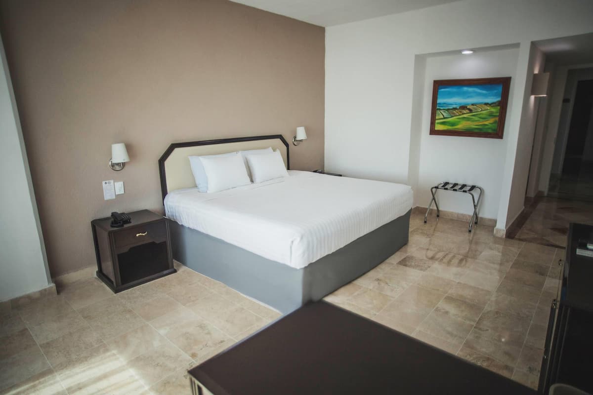 A bedroom with a large bed, a nightstand, a desk, and a painting on the wall.