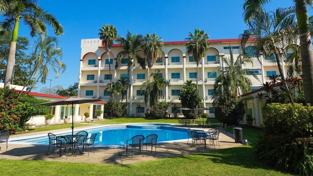 Un hotel con piscina, mobiliario exterior y palmeras.