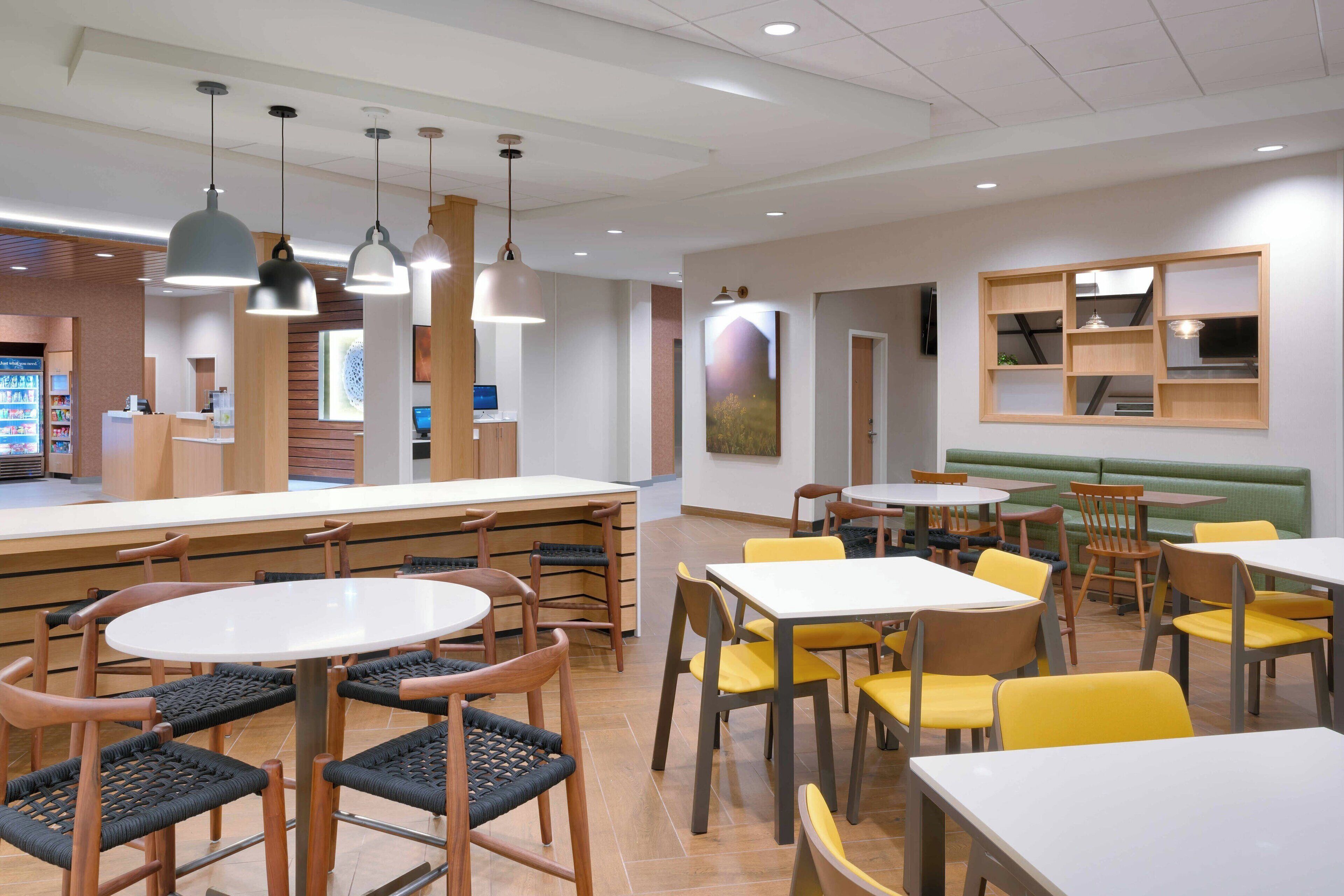 A modern dining area with round tables and chairs, a counter with a cash register, and a wall-mounted shelf with decorative items.