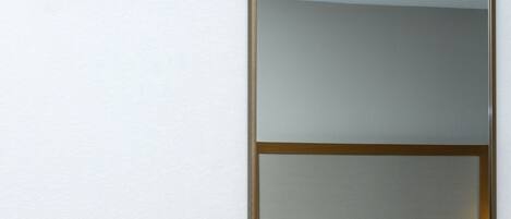 A hotel room with a bed, a mirror, a red emergency light, and a wall-mounted light switch.