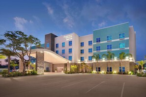 Un hôtel à plusieurs étages au design moderne, doté d’une entrée imposante avec un toit incurvé et d’une enseigne indiquant « Fairfield Inn & Suites Marriott ».