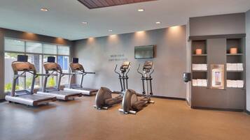 Centro de fitness com esteiras, elípticos e uma TV na parede.