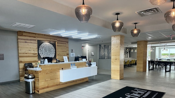 A hotel reception area with a wooden reception desk, a black doormat with the hotel name, and a modern interior design.