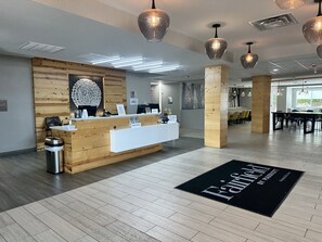 A hotel reception area with a wooden reception desk, a black doormat with the hotel name, and a modern interior design.