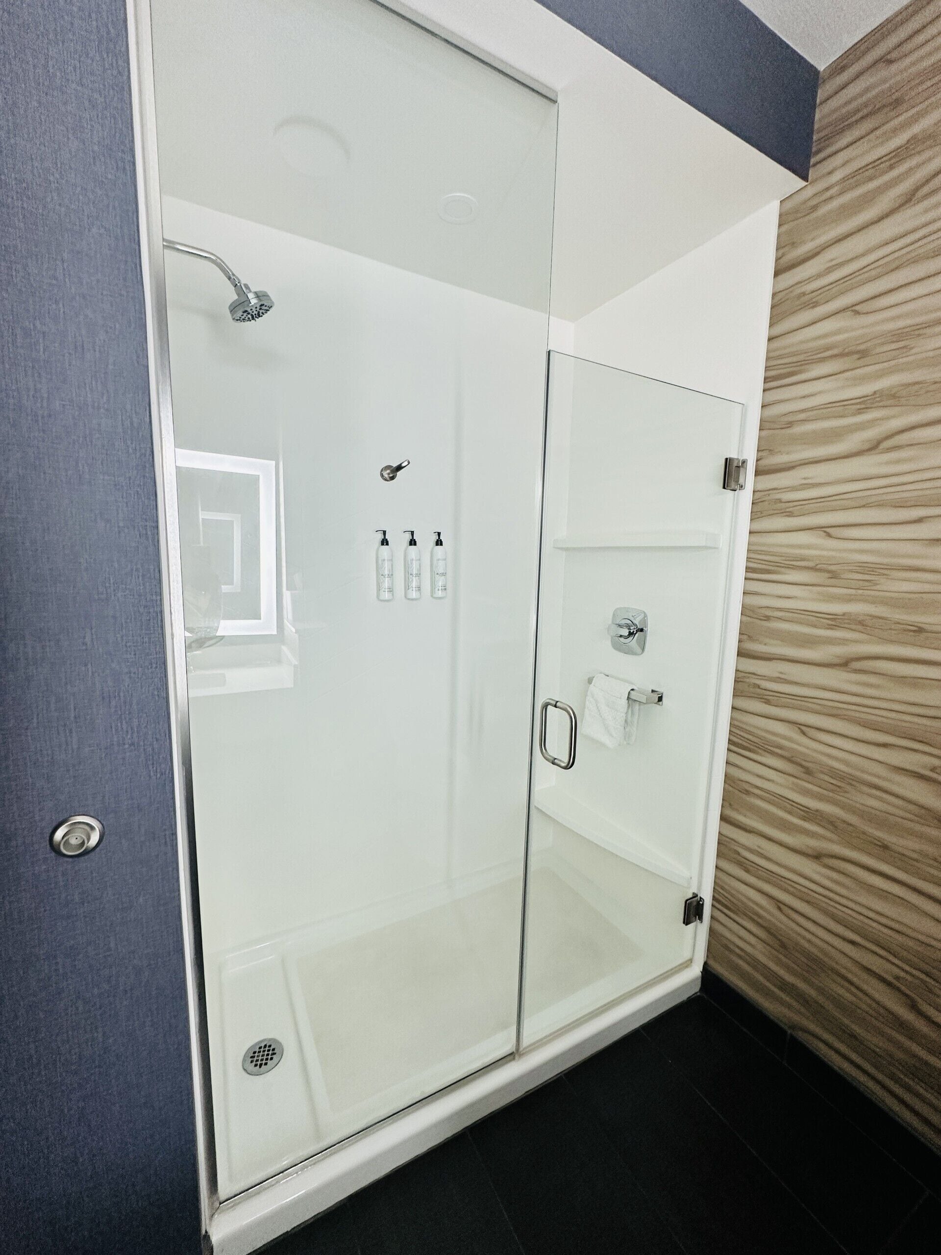 A modern bathroom with a glass shower enclosure, a towel rack, and a wooden wall panel.