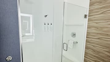 A modern bathroom with a glass shower enclosure, a towel rack, and a wooden wall panel.