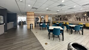 A modern restaurant with wooden flooring, blue and yellow chairs, and a mural of trees on the wall.
