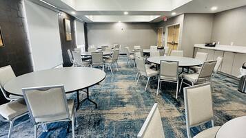 A conference room with round tables and chairs, a carpeted floor, and a white ceiling with recessed lighting.