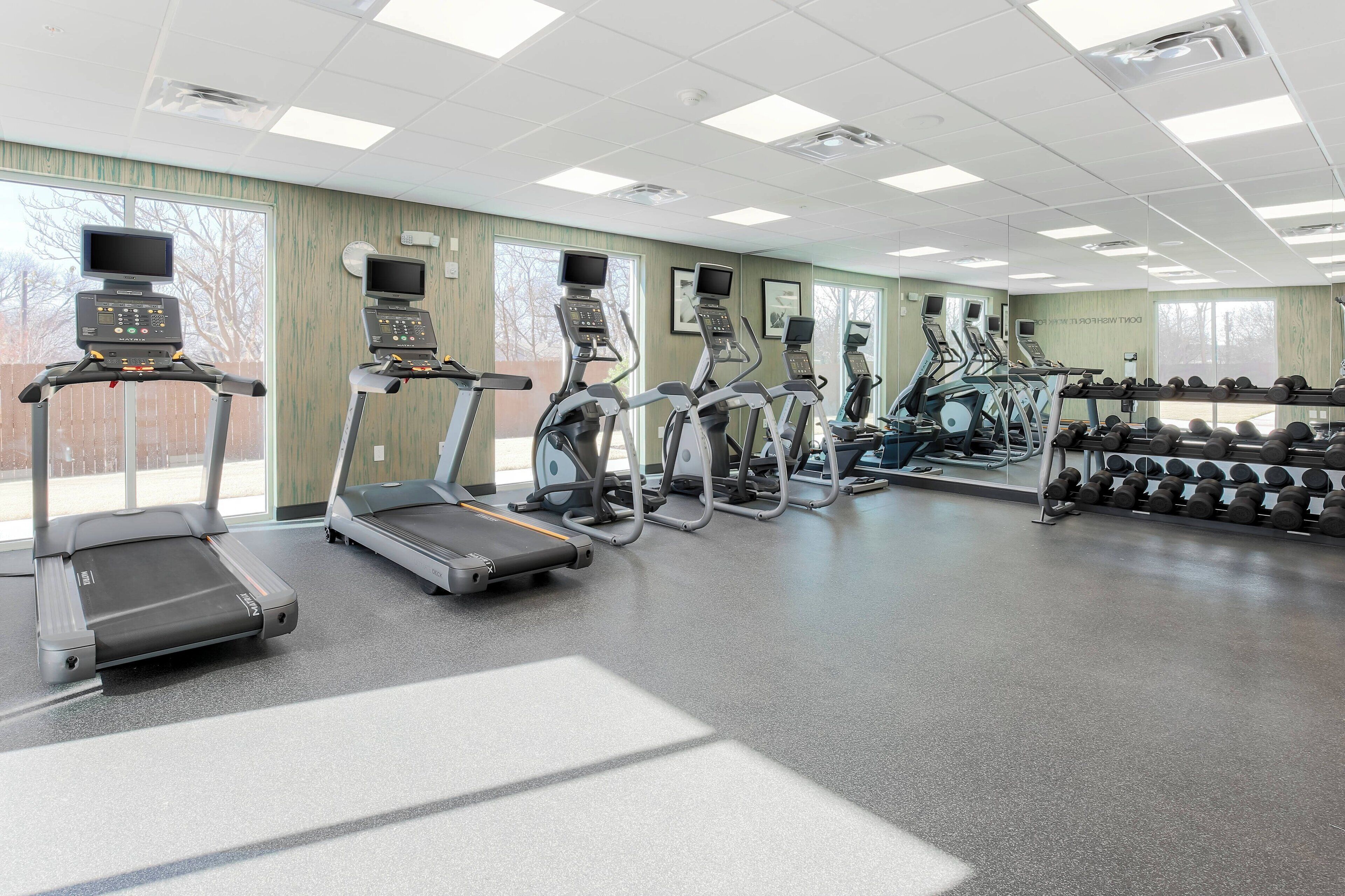 Een sportschool met loopbanden, elliptische trainers en een dumbbellsrek.