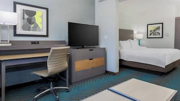 A hotel room with a desk, chair, television, bed, and artwork on the walls.