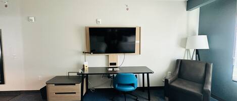 A hotel room with a bed, a desk with a chair, a television, and a lamp.