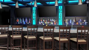 A bar area with wooden chairs, a bar counter with various bottles, and two large screens. - TownePlace Suites by Marriott McAllen Edinburg (Edinburg)