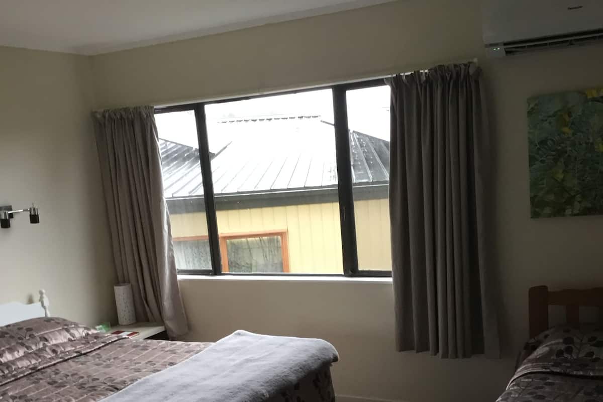 Ein Zimmer mit zwei Betten, einem fensterbelaubten Fenster, einer Klimaanlage und einer Wandleuchte.
