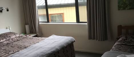 Een kamer met twee bedden, een raam met gordijnen, een airconditioner en een wandlamp.