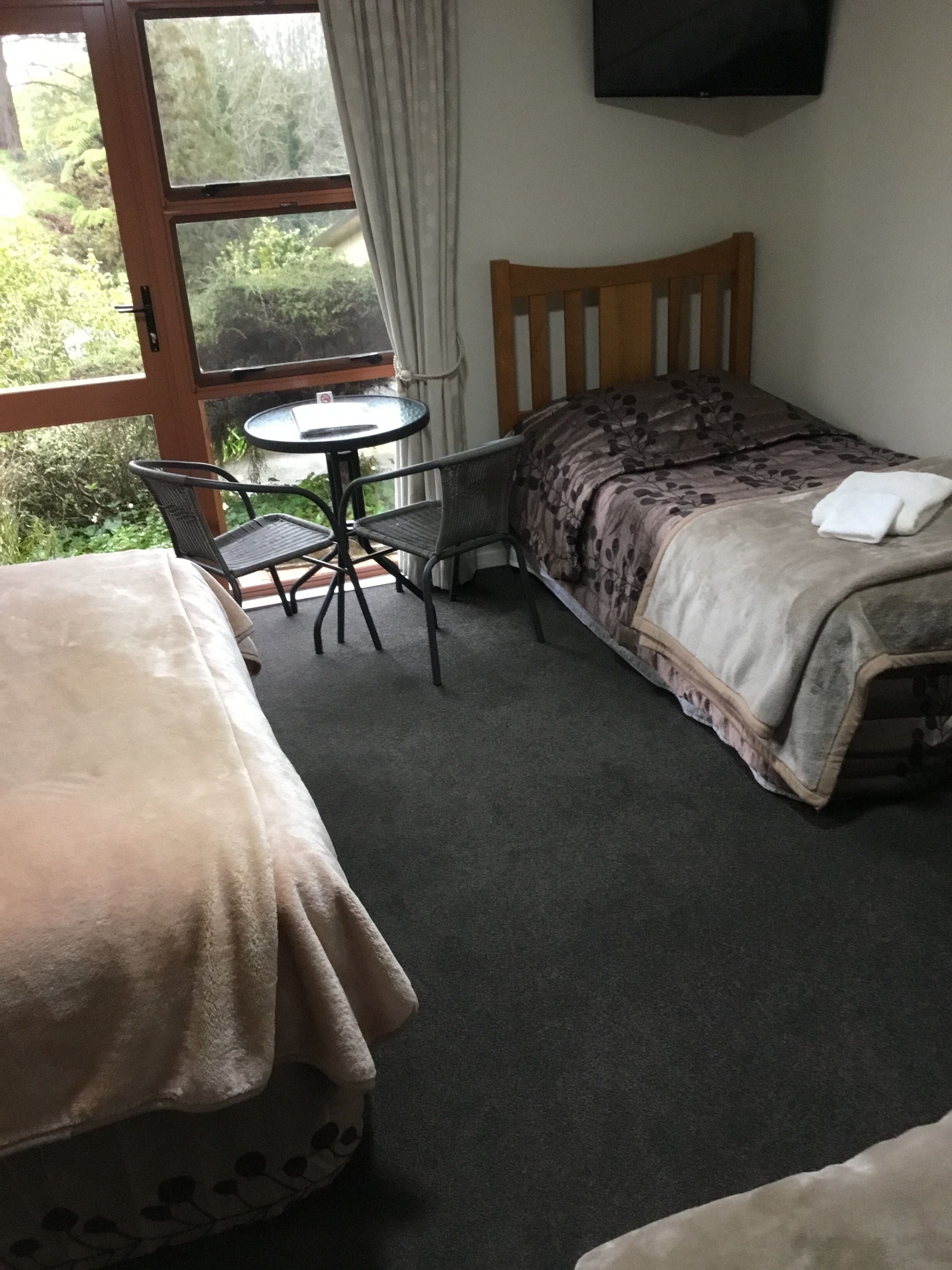 A room with two beds, a small round table, and a TV mounted on the wall.