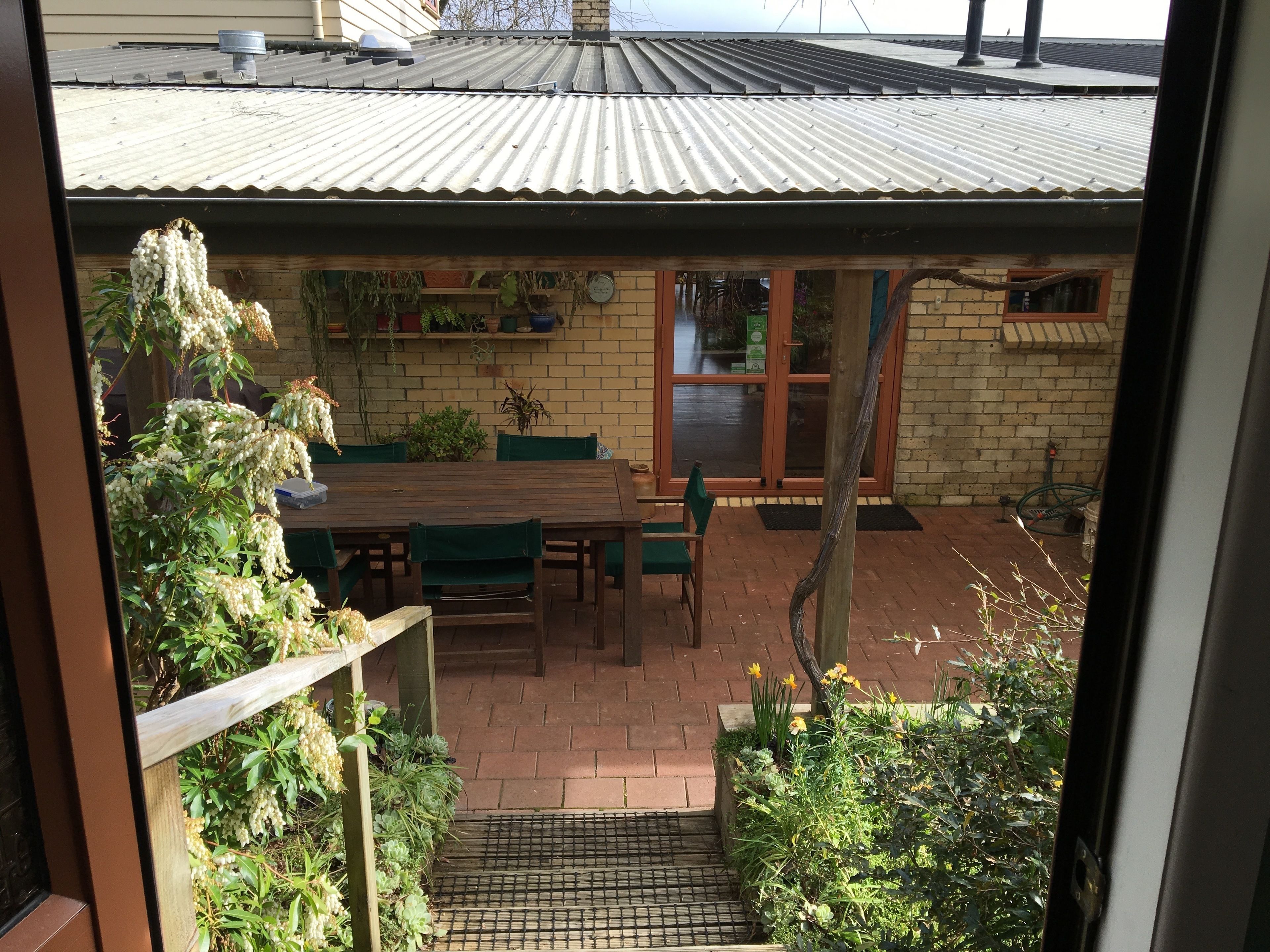 A patio with a wooden table and chairs, surrounded by potted plants and a brick wall.