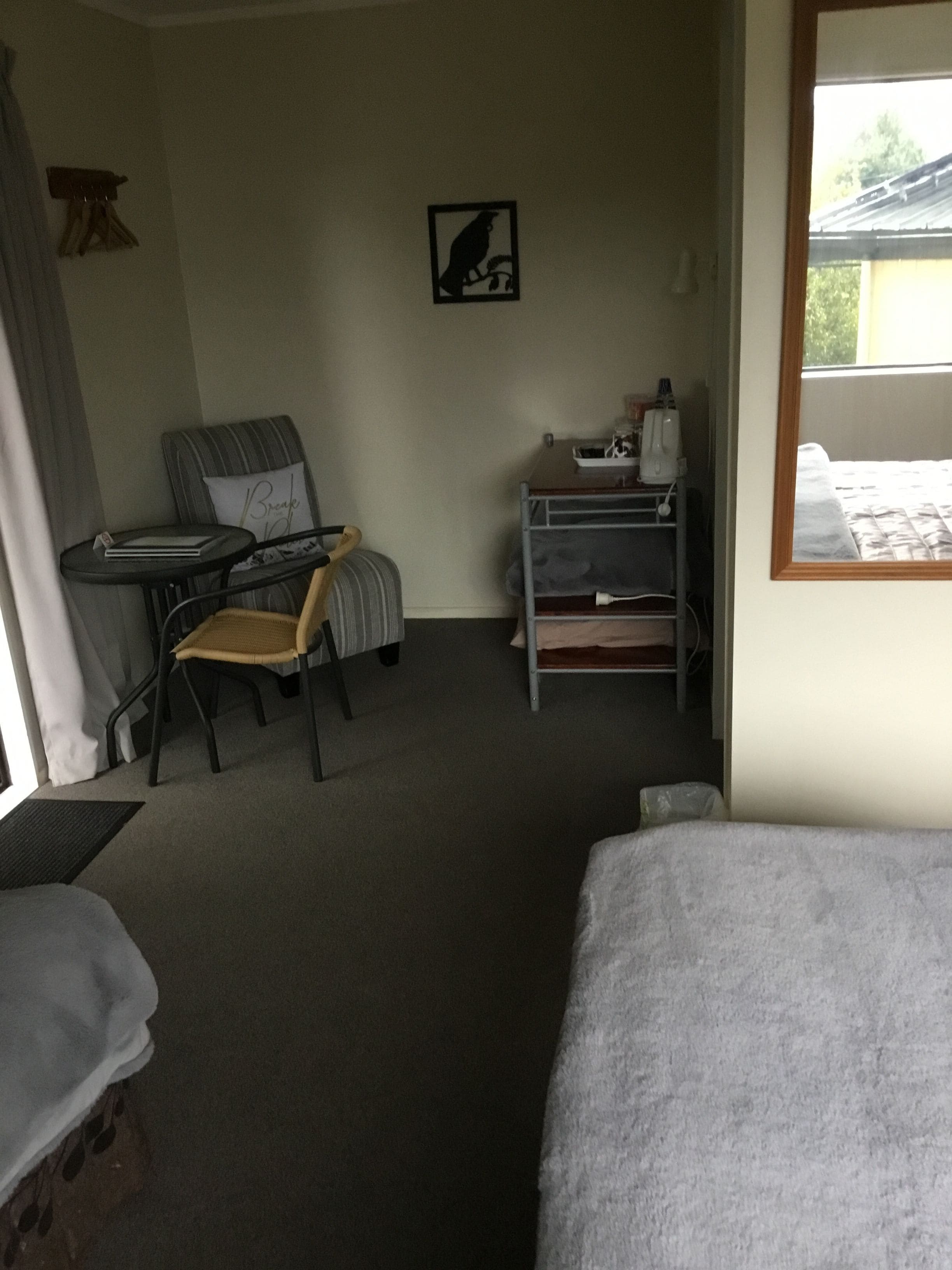 A hotel room with a bed, a desk with a chair, a small table, a chair, a picture on the wall, and a window.