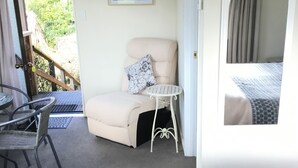A cozy room with a beige sofa, a small round table, and a chair. There's a window with curtains, a framed photo on the wall, and an air conditioning unit above. - Waitomo Caves Guest Lodge (Waitomo Caves)