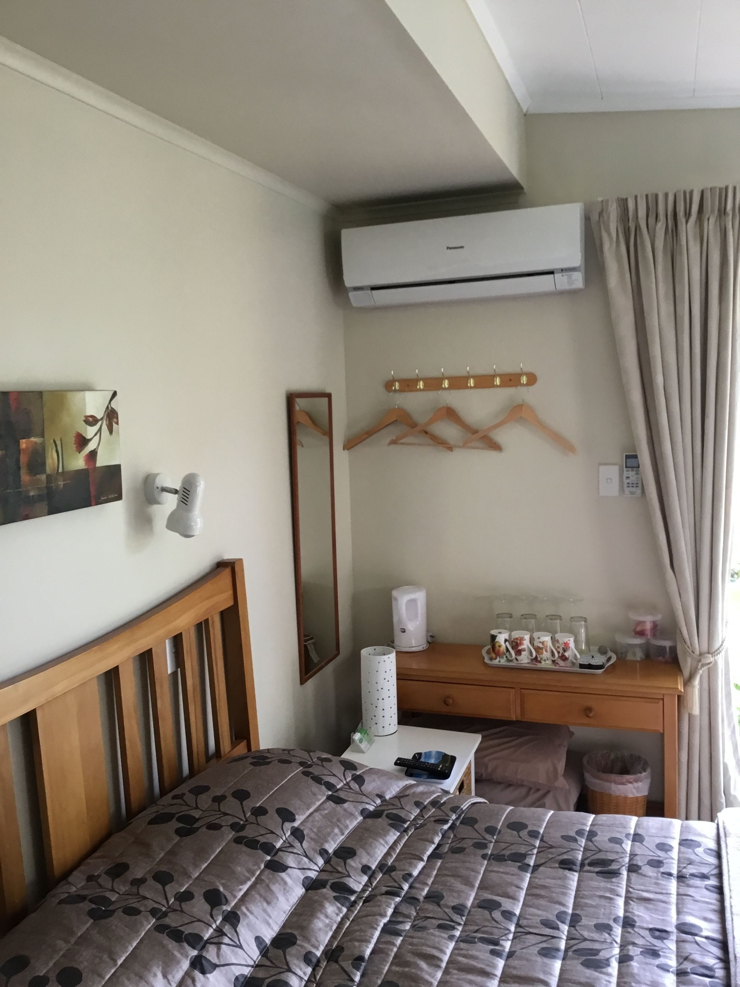 A bedroom with a bed, a dresser, a mirror, an air conditioner, and a window with curtains.