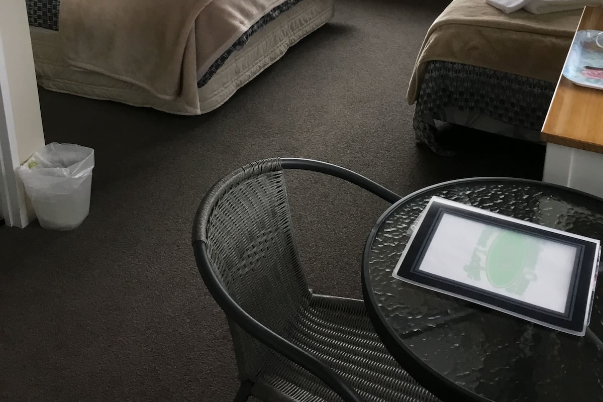 Ein Hotelzimmer mit zwei Betten, einem Schreibtisch mit Computer, einem Stuhl und Blick auf eine grüne Landschaft durch das Fenster.