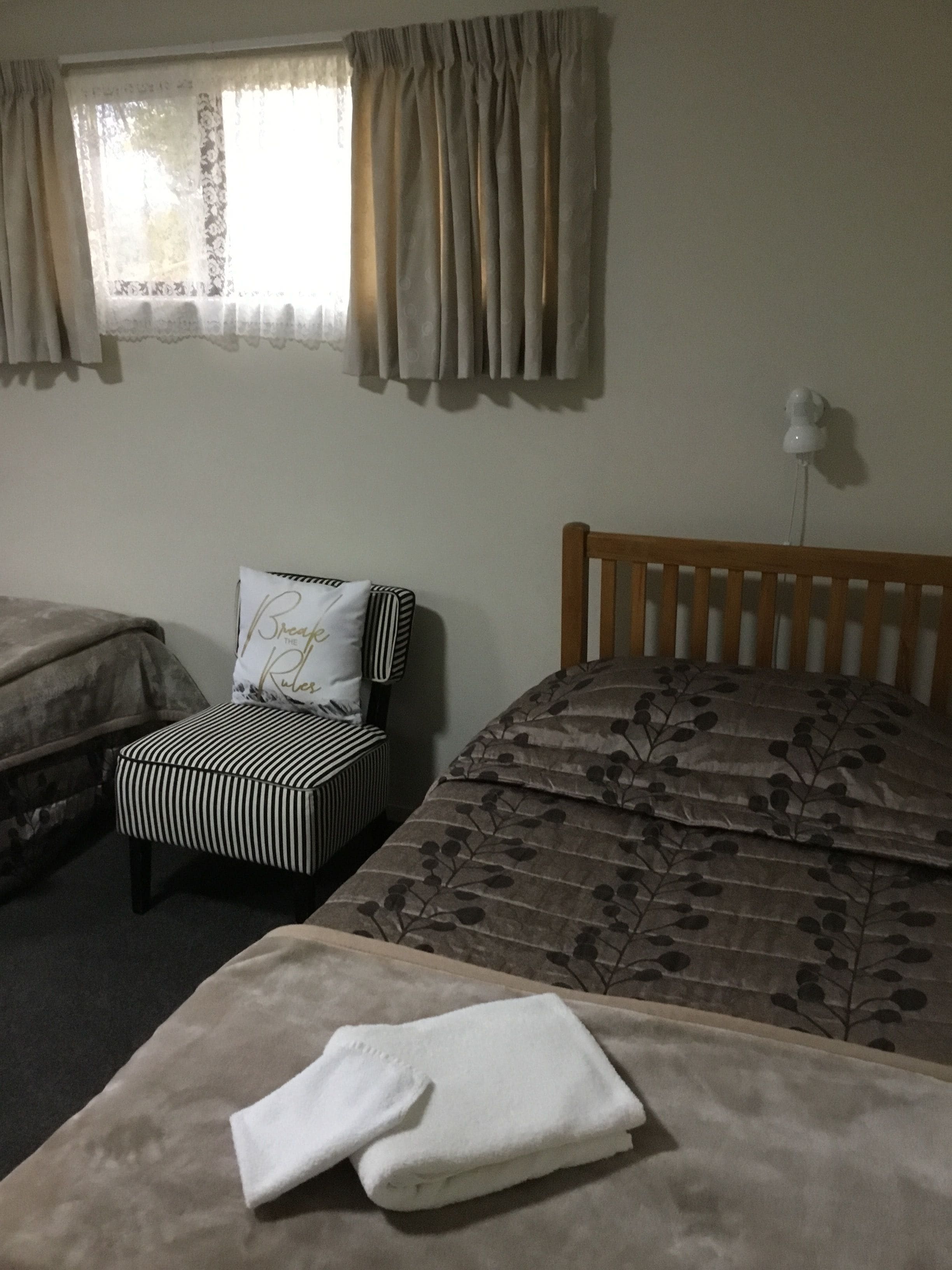 A room with two beds, a chair, and a window with curtains.