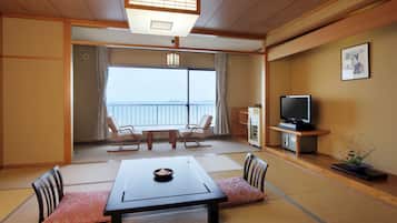 A traditional Japanese room with tatami flooring, a low table with cushions, a television, and a view of the sea.