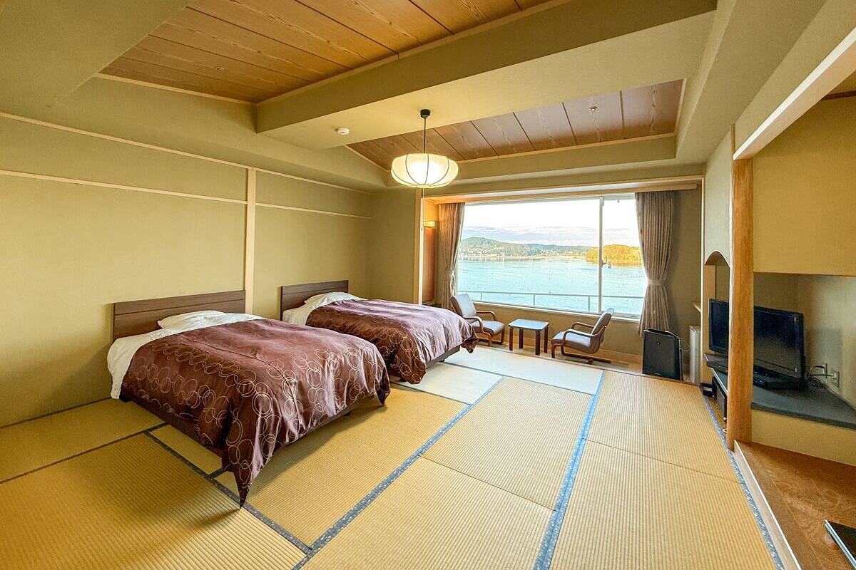 A hotel room with two beds, a TV, a view of the sea, and tatami mats on the floor.