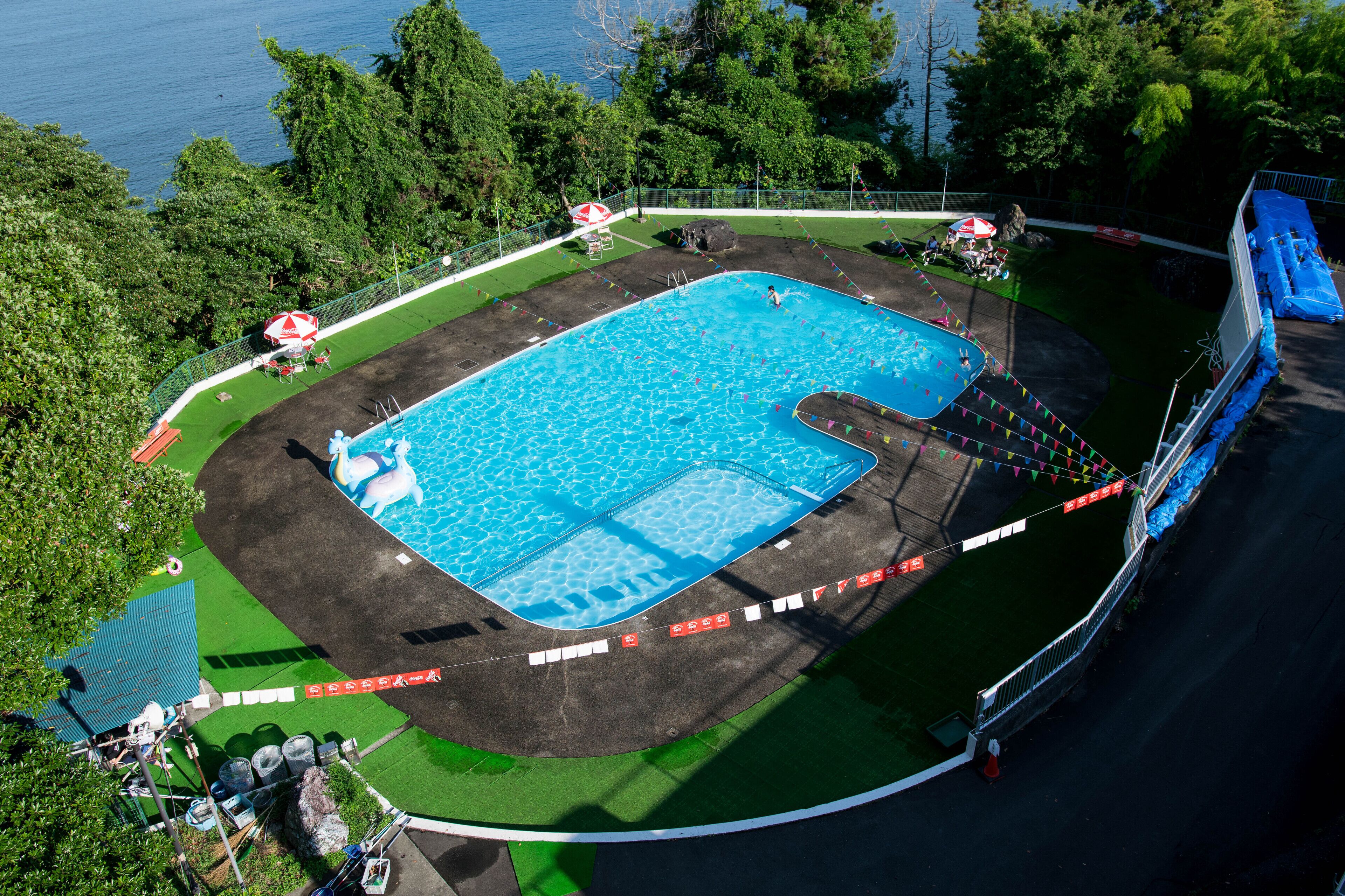 An aerial view of a swimming pool surrounded by green areas and a body of water.