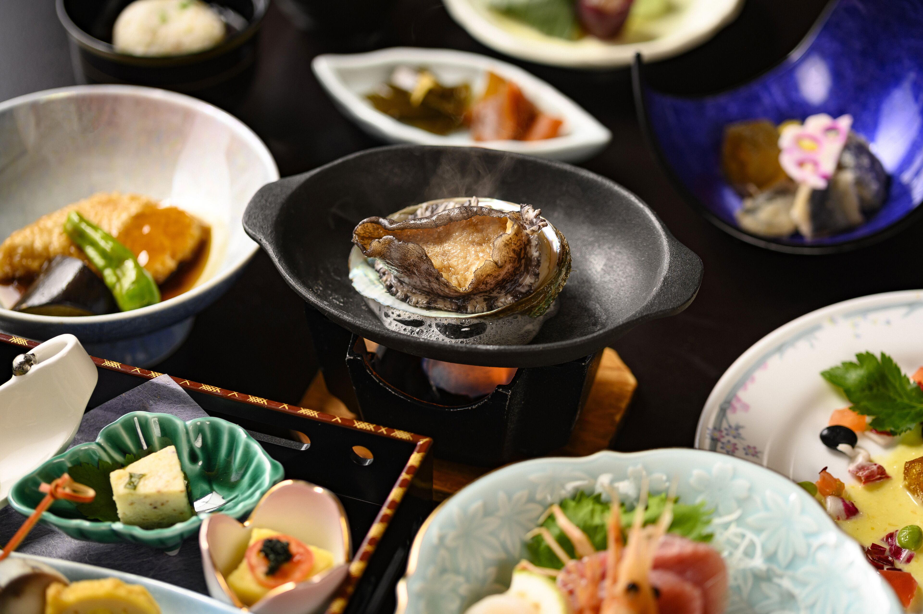 A variety of dishes on a table, including a bowl of soup, a plate with a piece of meat, and several small dishes with different foods.