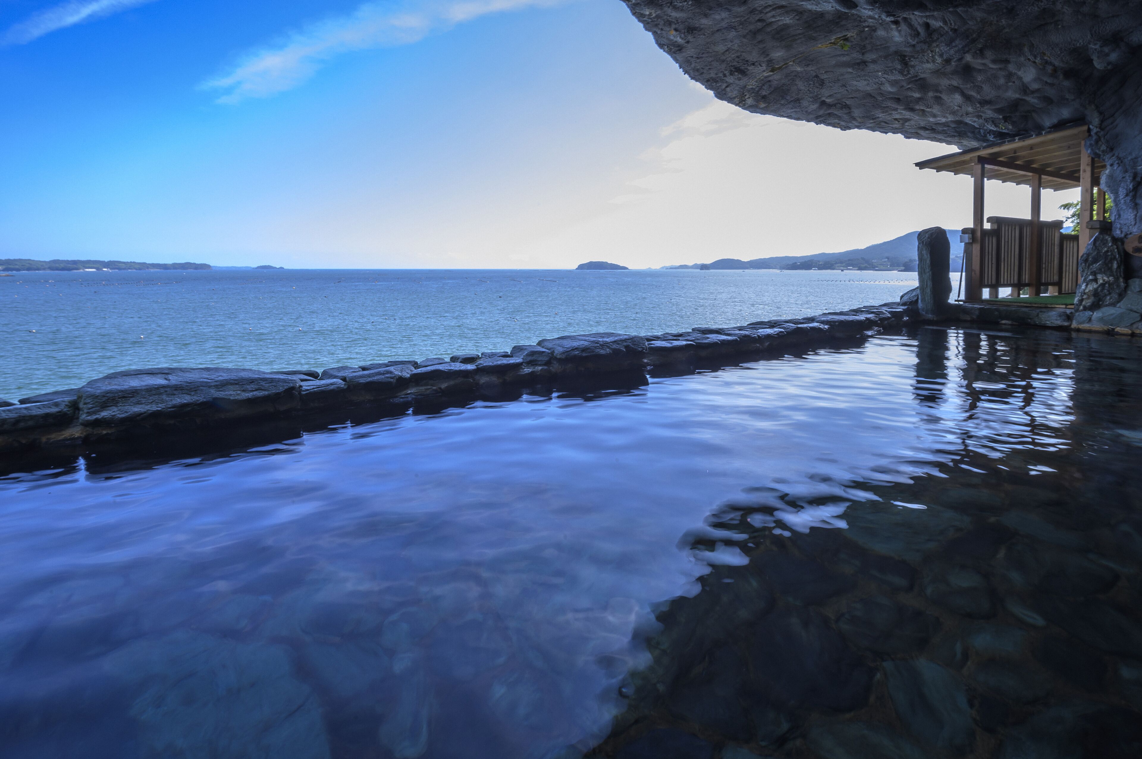 A coastal scene with a wooden structure built into a rock formation, overlooking a calm sea.