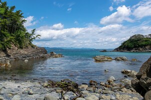 Una costa rocosa con aguas cristalinas, árboles y montañas a lo lejos.